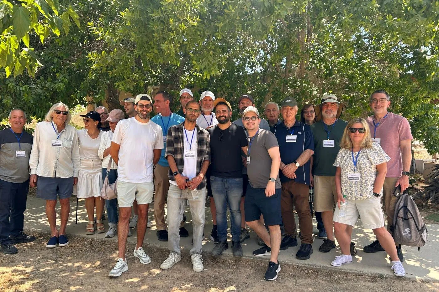 A group of mission participants wearing name badges pose together under trees