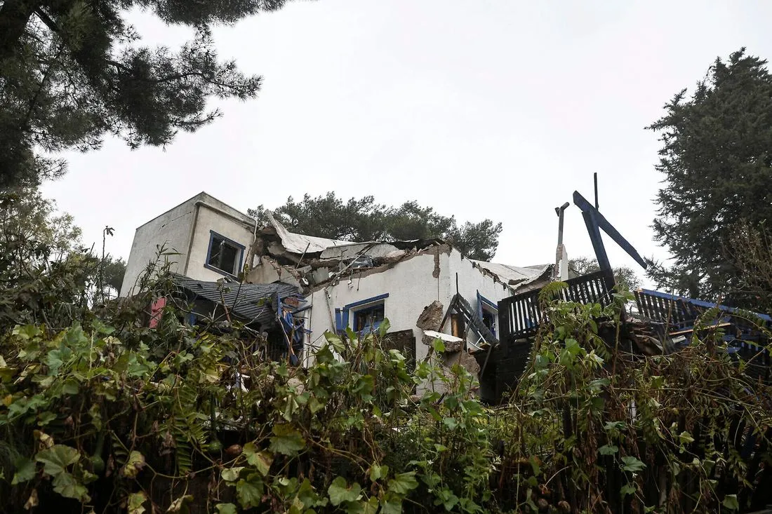 A heavily damaged house among trees, its roof and balcony torn open