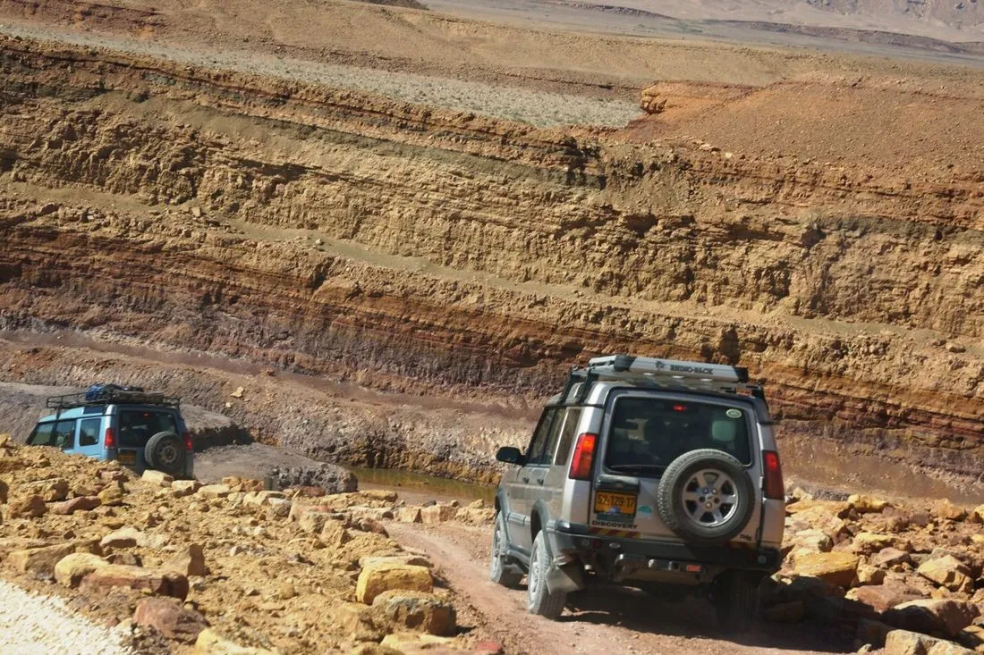 Two jeeps on a rocky track below layered desert cliffs